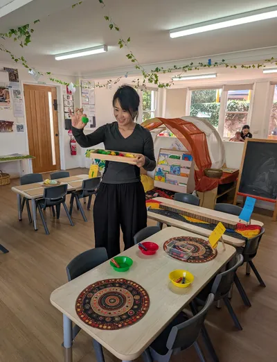 Educator setting up an activity at child-height tables in the Eastwood Blessings playroom