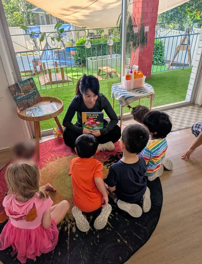 Educator reading a picture book to a group of children on the rug at Eastwood Blessings